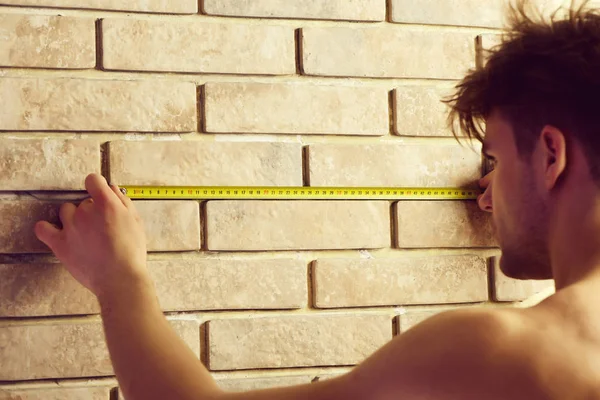 Man measures wall with measuring tape.