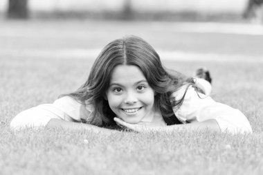 Sakin ol ve rahatla. Okullu mutlu çocuk yeşil çimlerin üzerinde yatıyor. Küçük kız resmi moda bakışlarıyla gülümsüyor. Küçük okul çocuğunun güzel görünüşü