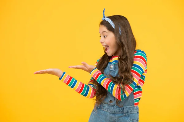 Girl demonstrate product. Promoting product for kids. Launching product. Advertisement concept. Product presentation. Kid happy smiling face show something on open palm copy space yellow background — ストック写真