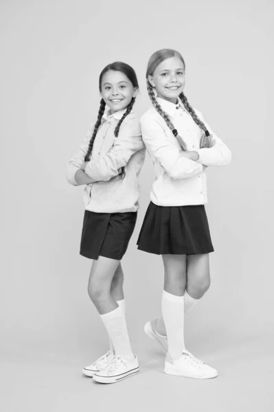 Insieme dai tempi della scuola. istruzione. Torniamo a scuola. alla moda bambino. Amicizia e sorellanza. ragazze felici in uniforme scolastica. ragazzine intelligenti su sfondo giallo. giorno della conoscenza. felicità infantile — Foto Stock