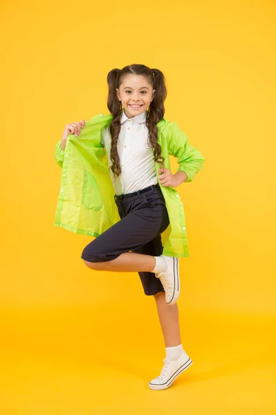 Waterproof concept. Small schoolgirl wear water resistant clothes for rainy day. Cute schoolgirl feel protected for spring weather. Adorable child. Happy schoolgirl wear raincoat on yellow background — Stock Photo, Image