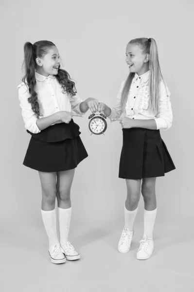 Gardez vos élèves en sécurité et à l'heure. Jolies petites filles tenant horloge rétro pendant le temps de l'école sur fond jaune. Petit enfant tenant le réveil. Il est temps d'apprendre. Horloge scolaire et solution de temps — Photo