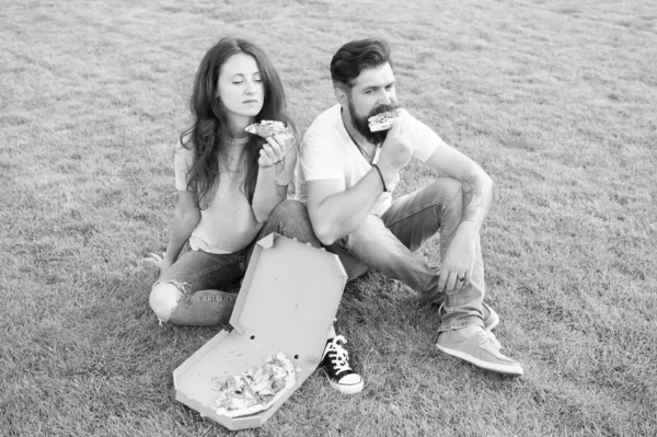 Summer picnic easy and quick ideas. Fast food. Bearded man and woman enjoy cheesy pizza. Couple in love dating outdoors with pizza. Hungry students sharing food. Couple eating pizza relaxing on lawn