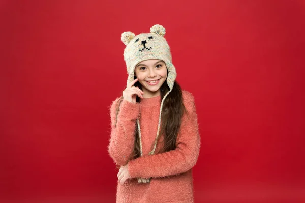 Felicidad y alegría. Traje de invierno. Un niño pequeño usa un sombrero de punto. Pequeña niña accesorio de moda de invierno. Niño pequeño pelo largo usar sombrero fondo rojo. Lindo modelo disfrutar del estilo de invierno. Adorable oso pequeño — Foto de Stock