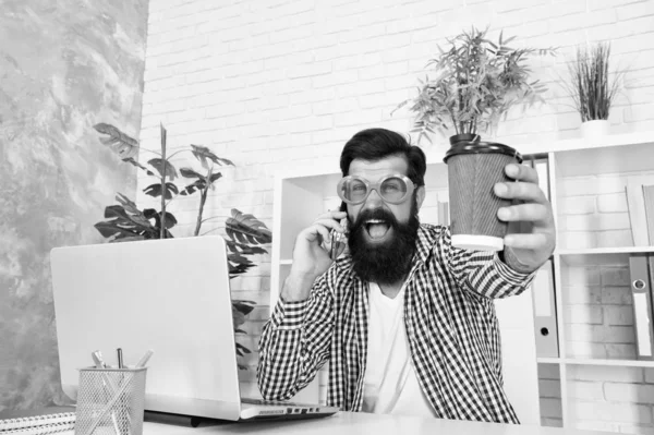 Ordering one more cup of drink by phone. Crazy man working on laptop with cup of hot drink. Bearded man in funky glasses enjoying his drink break in office. Tasty drink recipe — Stock Photo, Image