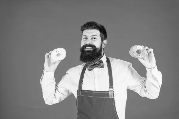 Carbohidratos y calorías. Barbudo alegre hombre bien arreglado vendiendo donas. Propietario de panadería. Negocio de panadería. Productos horneados. Dulces y pasteles. Comida chatarra. Hipster panadero barbudo comer donas. Panadería de rosquillas —  Fotos de Stock