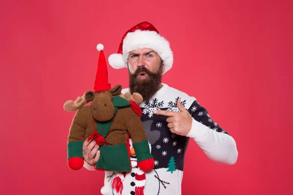 冬休みだ。クリスマスの準備の概念。贈り物を買って。冬の販売とショッピング。冬のごちそう。トナカイのおもちゃ。サンタの帽子の男はクリスマスプレゼントの赤い背景を保持します。ヒップスター陽気な顔冬のセーター — ストック写真