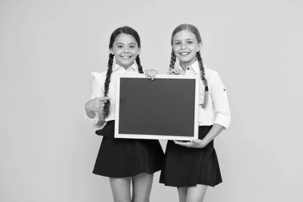 Schrijftijd. Kleine meisjes houden zwarte schrijfoppervlak op gele achtergrond. Kleine kinderen wijzend vinger op schoolbord voor het schrijven van informatie. Blanco bord voorschrijven, ruimte kopiëren — Stockfoto