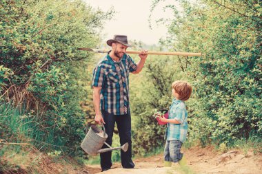 Ağaç dikme geleneği. Bahçedeki küçük yardımcı. Çiçek ekiyorum. Bitki yetiştiriyorum. Çocuk ve babası doğada sulama tenekesi ve kürekle. Baba oğluna bitkileri yetiştirmeyi öğretiyor. Ağaç dikme günü. Ağaç dikiyorum.
