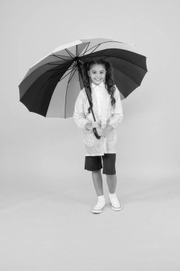 Eğer suya dayanıklı giysiler varsa Yağmur çok kötü değildir. Kaygısız kız öğrenci renkli şemsiye su geçirmez yağmurluk giymek. Sonbahar yağmuru. Parlak aksesuarlar ile okula yağmurlu gün daha eğlenceli gidiyor