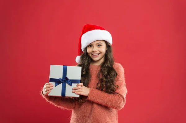 Want to put it. best christmas offer. little girl hold present box. happy new year gift. christmas holiday party. small girl in santa hat. cheerful child red wall. kid shopping sales. xmas boxing day — Stock Photo, Image