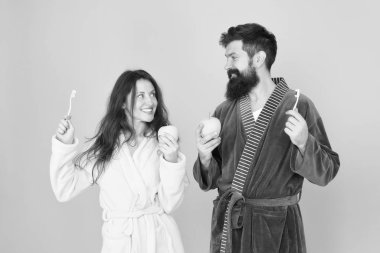 Sabah kişisel bakım. Bornoz giymiş çiftler. Sakallı adam ve kız sağlıklı bir gülümseme. Aile çifti diş fırçasıyla elma tutuyor. Sağlıklı ve güçlü dişlere sahip olmak. Sağlıklı alışkanlıklar