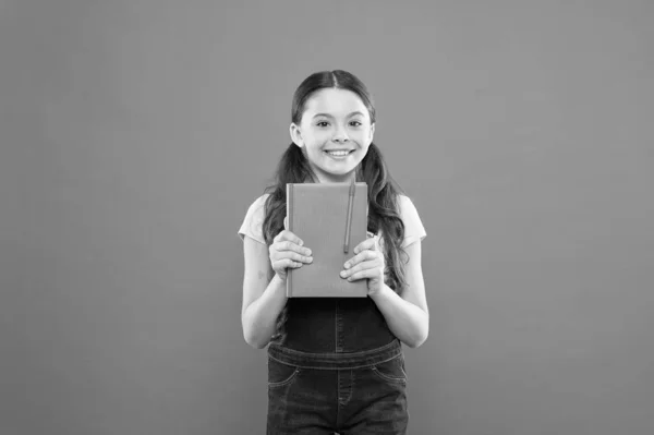 Παιδική λογοτεχνία. ευτυχισμένο κοριτσάκι με σημειωματάριο. μάθημα λογοτεχνίας. σχολείο κορίτσι διαβάζουν βιβλίο για πορτοκαλί φόντο. ποίηση και μυθιστόρημα. της σύγχρονης εκπαίδευσης. γράφοντας σημειώσεις. Παιδικό ημερολόγιο. πίσω στο σχολείο — Φωτογραφία Αρχείου
