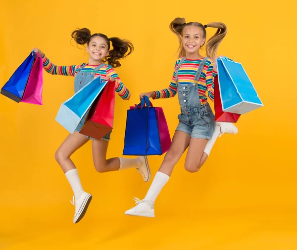 작은 아이들은 무거운 쇼핑백을 들고 있습니다. 선물을 많이 팔고 있어요. 쇼핑하는 아이들 이 행복하겠지. 어린 소녀들이 아끼는 패키지입니다. 자유 낙하 !. 여름 쇼핑. 소비자 컨셉. 휴가 구매 절약 — 스톡 사진