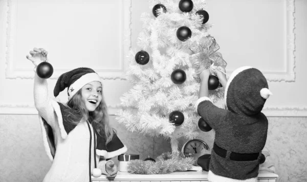 孩子们在圣诞老人的帽子装饰圣诞树。家庭传统概念。孩子们一起装饰圣诞树。男孩和女孩装饰树。兄弟姐妹们忙着装饰。珍爱人的节日活动 — 图库照片