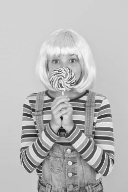 Tatlıyı. Küçük çocuk lolipop şeker sarısı arka planda. Çubuğun üzerinde gökkuşağı kıvrımlı şekerlemeleri olan küçük bir kız. Tatlı çocuk şekerli tatlının tadını çıkarıyor. En iyi şekerci