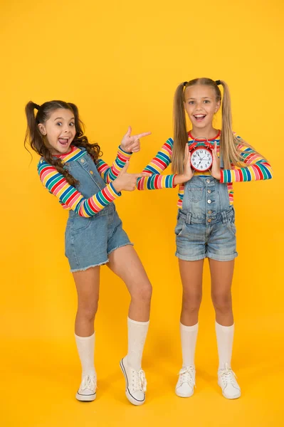 As crianças quebram conceito. duas meninas alegres segurar despertador. de volta à escola. Hora de Verão. disciplina e gestão do tempo. meninas adolescentes parede amarela. crianças relógio vintage. contagem para a hora do almoço — Fotografia de Stock