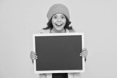 Bilgi eğitim materyalleri. Küçük mutlu çocuk sarı arka planda eğitim için boş tahtayı tutuyor. Zorunlu ilkokul eğitimi. Kamu eğitim programı, kopyalama alanı