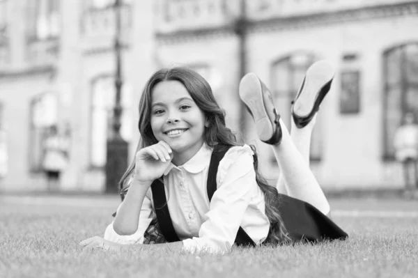 Its that time of year again. Relaxed schoolchild. Happy schoolchild relax on green grass. Small schoolchild enjoy school time outdoor. Little schoolchild with long brunette hair smile in formal wear