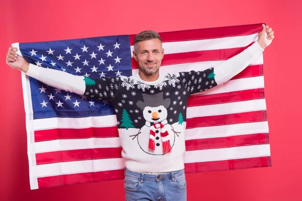 Vrijheid voor altijd. Knappe man vieren wintervakantie rode achtergrond. Hij draagt een wintertrui. Vrolijk kerstfeest en gelukkig nieuwjaar. De beste wensen. Wintervakantie. Rijpe man met Amerikaanse vlag — Stockfoto