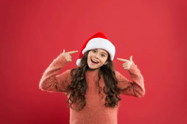 Menina adorável com cabelos longos encaracolados usar Papai Noel chapéu fundo vermelho. A contar dias até ao Natal. Festa de Natal. Convite de Natal. Conceito de positividade. Bom humor. Tradições de inverno — Fotografia de Stock