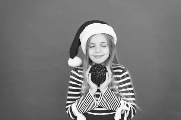 Toma tu regalo y pide un deseo. Niña sostiene la bola de regalo roja. Niño pequeño con aspecto de santa. Regalo de Navidad. Regalo de Navidad. Regalo de año nuevo — Foto de Stock