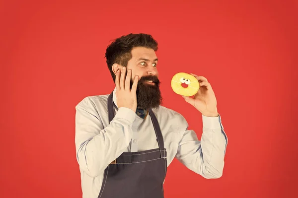 Glucides régime au gluten. Homme barbu bien entretenu dans un tablier vendant des beignets. Nourriture aux beignets. Hipster boulanger tenir des beignets. Enthousiaste. Un beignet glacé. Des pâtisseries. Bonbons et gâteaux. De la malbouffe. Calories de beignets — Photo