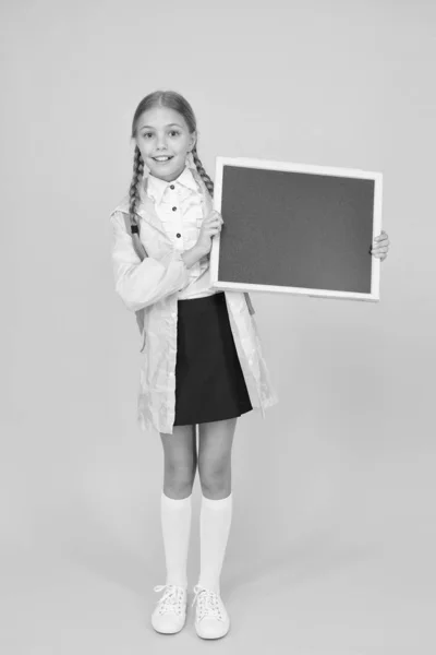 Placement of ad. Little child hold blank blackboard for information on yellow background. Small schoolgirl smile with tidy information board. Sharing happy information. Your information, copy space — Stock Photo, Image