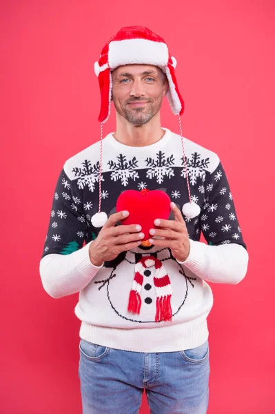 - Szeretlek. Jóképű ember ünnepli téli ünnepek piros háttér. A fickó téli pulóvert visel. Boldog karácsonyt és boldog új évet! Minden jót. Téli vakáció. Érett férfi kalapban mosolygós arc sörte — Stock Fotó