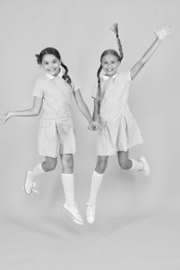 Eğleniyorum. Eski moda. Klasik tarzda çocuklar. Eski usul. Mutlu arkadaşlar sarı arka planda zıplarlar. Çocuk modası güzeli. çocukluk mutluluğu. Kardeşlik kavramı. Okul üniformalı küçük kızlar