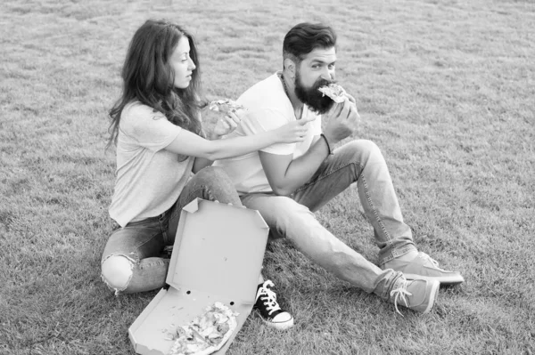 Pareja comiendo pizza relajándose en el césped verde. Entrega de comida rápida. Barbudo hombre y mujer disfrutar de pizza con queso. Pareja enamorada saliendo al aire libre con pizza. Estudiantes hambrientos compartiendo comida. Puro disfrute. —  Fotos de Stock