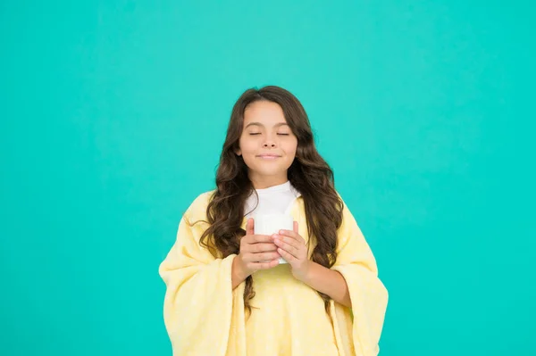 Drink well, live well. little girl drink cocoa or milk before sleeping. cosy and fluffy pajama. feeling comfortable at home. happy girl with tea cup. good morning drink. small kid blue background