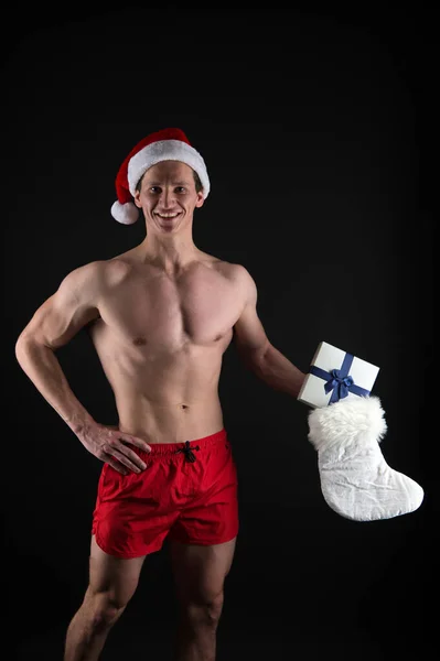 Çorap malzemeleri. Kaslı adam Noel Baba şapkası takıyor. Siyah arka planda vücut geliştirici. Kış tatili Kaslı sporcu yeni yılı kutluyor. Noel ruhu. Noel geleneği. Mutlu Noeller. — Stok fotoğraf