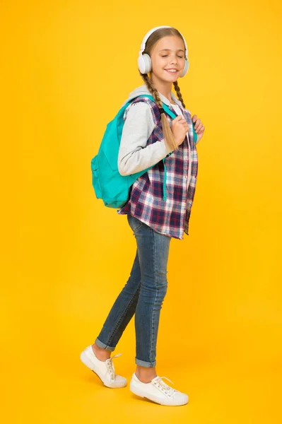 Hipster κορίτσι φροντίδα σακίδιο. μαθητριούλα casual στυλ κρατήσει σχολική τσάντα. Φθινοπωρινή παιδική μόδα. παιδί ακούει μουσική ακουστικά. παιδική εκπαίδευση και ανάπτυξη. Χαρούμενη ημέρα των παιδιών. ακουστικό βιβλίο — Φωτογραφία Αρχείου