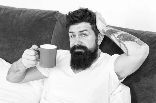 Tune in to new day. Morning awakening better with cup coffee. Relax and rest. Humanity runs on coffee. Man brutal handsome hipster relaxing bedroom drink coffee. Bearded guy enjoy morning coffee