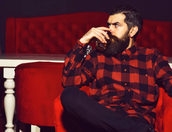 Hombre barbudo hipster sosteniendo vaso de whisky en silla roja — Foto de Stock