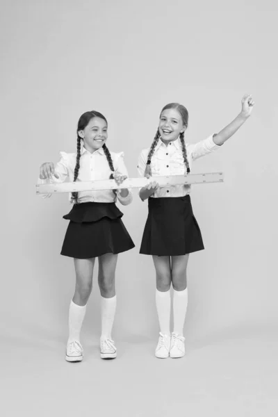 Zelfverzekerde leerlingen. gelukkige kleine meisjes studeren wiskunde. studenten gebruiken gele liniaal. stem disciplines. terug naar school. Wiskunde en geometrie. Kinderen in uniform meten. school vriendschap — Stockfoto