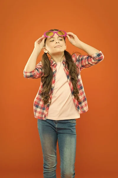 Destacando suas melhores características com óculos. Menina legal usando óculos com filtro de cor. Criança pequena com óculos de festa no fundo laranja. Criança pequena que parece confiante através de óculos de moda — Fotografia de Stock