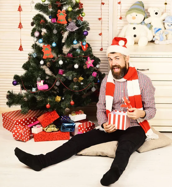 Le gars en chapeau et écharpe est assis près de l'arbre de Noël — Photo