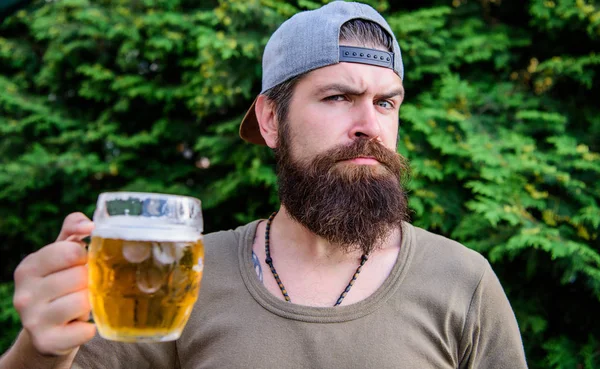 Спасаюсь от летней жары. Жестокий хипстер пьет освежающее пиво в летний день. Бородатый мужчина держит кружку пива на летней природе. Пьяница наслаждается летним временем — стоковое фото