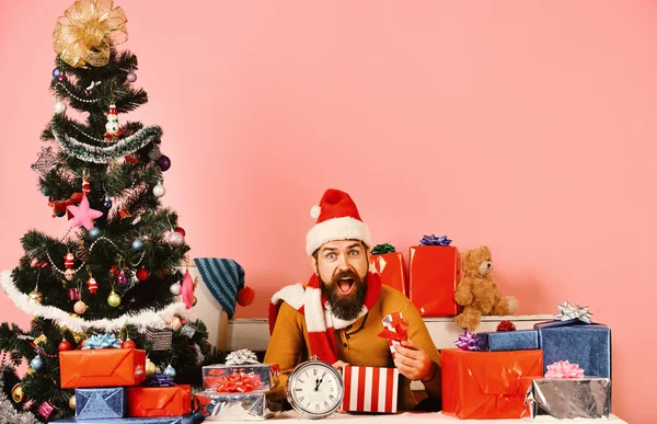 Weihnachtsmann öffnet Geschenke neben geschmücktem Baum auf rosa Hintergrund. — Stockfoto
