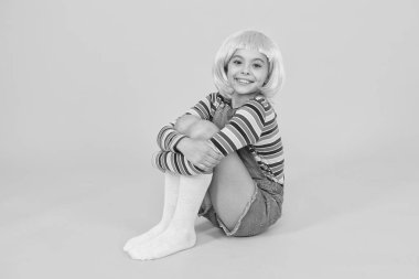 Şık ve yaratıcı. Mutlu çocuk şık kısa saç peruğu takıyor sarı arka plan. Küçük kız şık bir şekilde gülümsüyor. Şık bir kuaför salonu. Moda ve tarz