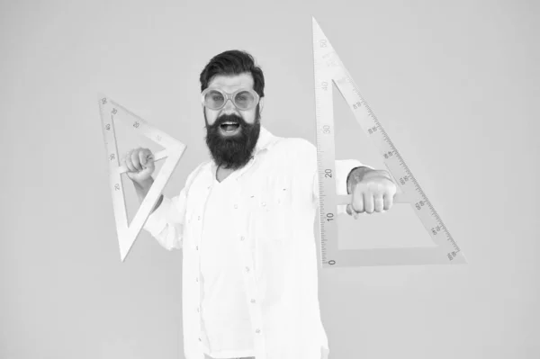 Making geometry fun. Funny hipster using geometrical tools at geometry. Geometry teacher holding triangles for school lesson on yellow background. Bearded man learning or teaching geometry — Stock Photo, Image