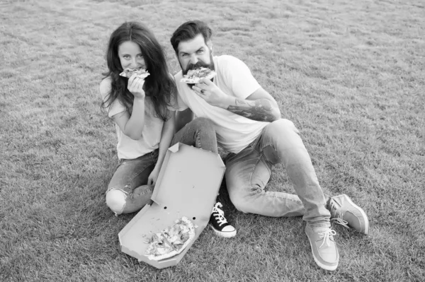 Hungry people. Simple happiness. Cheat meal. Couple eating pizza relaxing on green lawn. Fast food delivery. Bearded man and girlfriend enjoy cheesy pizza. Couple in love dating outdoors with pizza