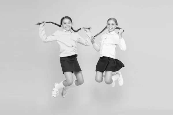 Feeling good fabulous hair. Cute small children with plaited hair jumping on yellow background. Happy little girls holding long hair braids in mid air. Braiding and styling your hair for school — Stock Photo, Image