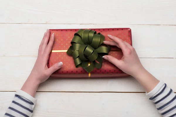 Female hands hold box wrapped in red paper with bow