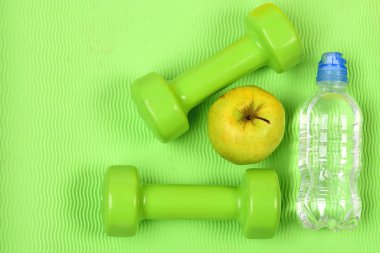 Halterler, elma ve su şişesi yoga minderinde.