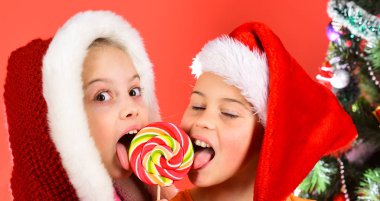 Kızlar lolipopu birlikte ısırır, yakın plan. Noel şapkalı kız kardeşler