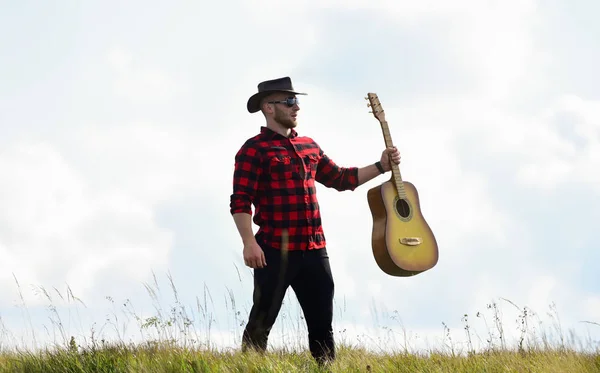 Country music concept. Guitarist country singer stand in field sky background. Country style. Summer vacation. Hiking song. Inspired country musician. United with nature. Handsome man with guitar