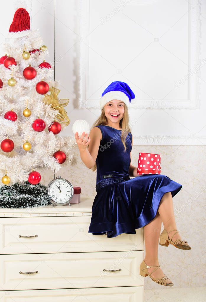 Child celebrate christmas at home. Kid girl sit near christmas tree hold gift box. Little girl santa hat excited about christmas gift or present. Time to open christmas gifts. Happy new year concept